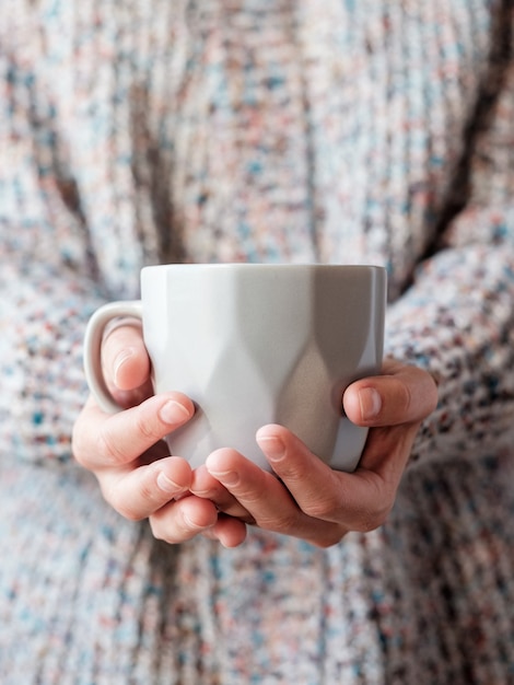 Eine Frau, die an einem kalten Tag einen Wollpullover trägt und eine Tasse warmen Tee in den Händen hält