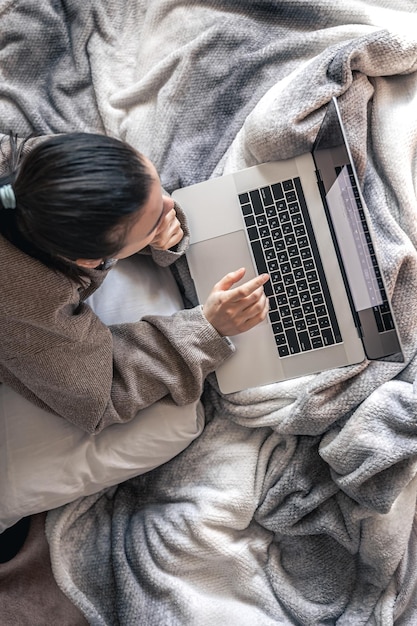 Eine Frau, die an einem Laptop arbeitet, während sie in der Draufsicht des Bettes liegt