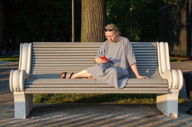 Eine Frau, die an einem Sommertag in einem Park sitzt, kauft online ein oder kommuniziert in Instant Messenger von ihrem Smartphone aus