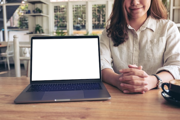 Eine Frau, die Arbeit mit Laptop mit leerem weißen Bildschirm auf Holztisch präsentiert