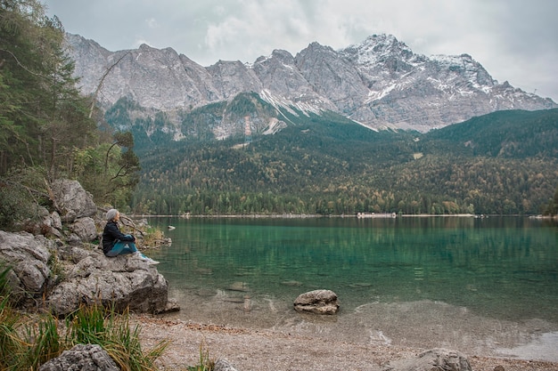 Eine Frau, die auf den Felsen nahe dem See sitzt. Alpen Deutschland.