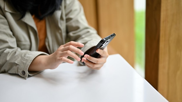 Eine Frau, die auf ihrem Telefon scrollt, während sie im Café sitzt und auf ihr Getränk wartet