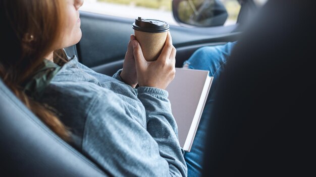 Eine Frau, die Buch hält und Kaffee im Auto trinkt