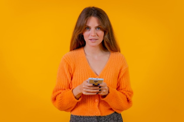 Eine Frau, die Dinge im Internet auf dem Handy auf einem Online-Shopping-Konzept mit gelbem Hintergrund betrachtet