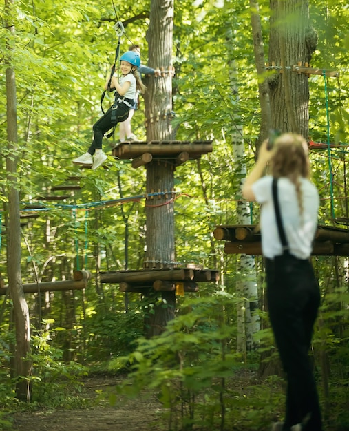 Eine Frau, die ein Foto von ihrer kleinen Tochter macht, die am Versicherungsgürtel im Wald hängt