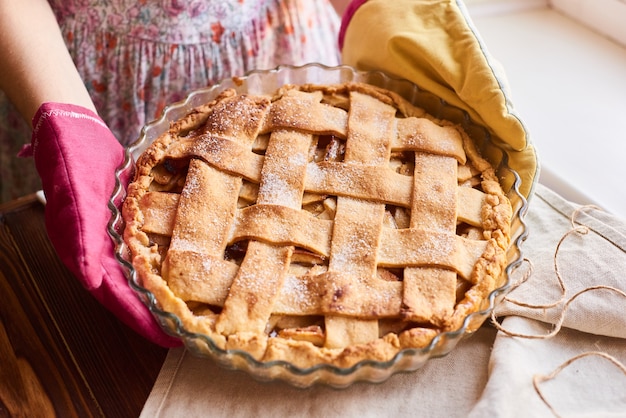 Eine Frau, die ein frisches Bratapfeltörtchen hält. Frau, die köstliche amerikanische Torte auf Tabelle setzt. die hausfrau in den küchenhandschuhen bringt den apfelkuchen auf den tisch.