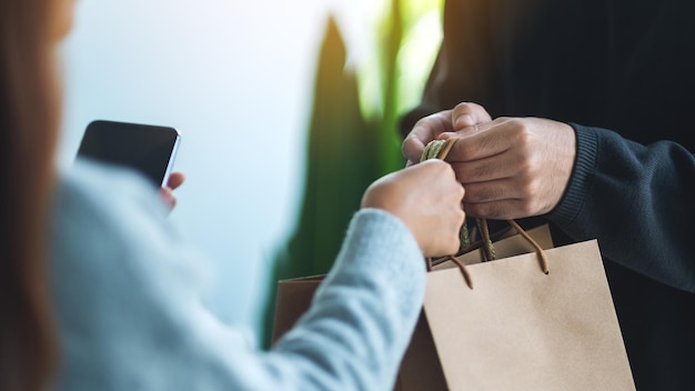 Eine Frau, die ein Handy hält und Einkaufstüten vom Lieferboten erhält