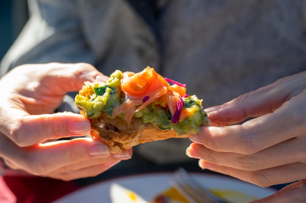 Foto eine frau, die ein lachs-avocado-sandwich isst, hält es in der hand und isst draußen mittagessen