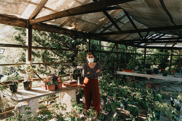 Eine Frau, die eine Maske trägt, die während eines super Sonnenuntergangs im Garten arbeitet, mit vielen Pflanzen und Blumen, die sie umgeben, mit Kopierraum