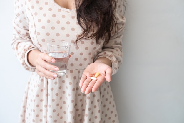 Eine Frau, die eine Medizin und ein Glas Wasser in der Hand hält