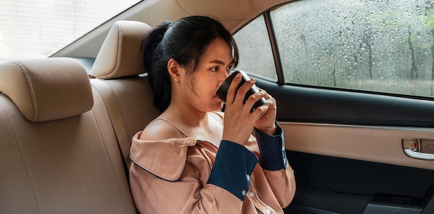 Eine Frau, die hinten in einem Auto sitzt und in einsamer Stimmung Kaffee trinkt