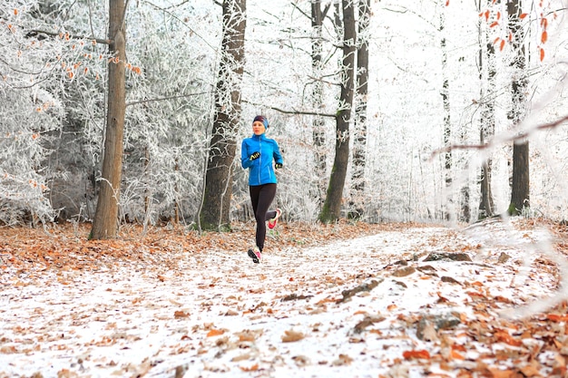 Eine Frau, die im Winter im Wald joggt, in voller Länge