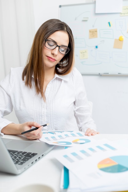 Eine Frau, die in einem Büro sitzt, arbeitet mit Finanzberichten und Diagrammen.