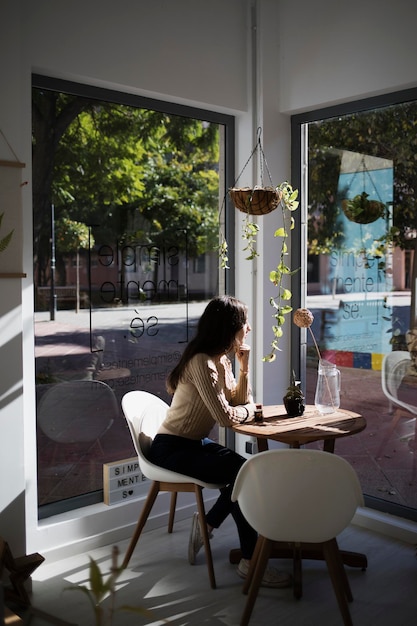 Eine Frau, die in einem Café sitzt, schaut aus den Fenstern. Die Sonne trifft ihr Gesicht