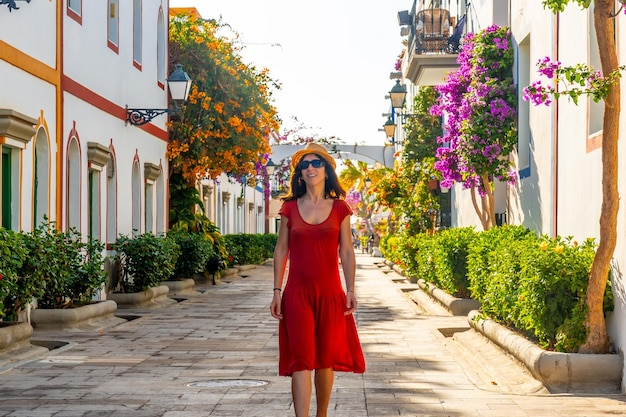 Eine Frau, die in einem roten Kleid im blumigen Hafen der Stadt Mogan im Süden von Gran Canaria, Spanien, spazieren geht