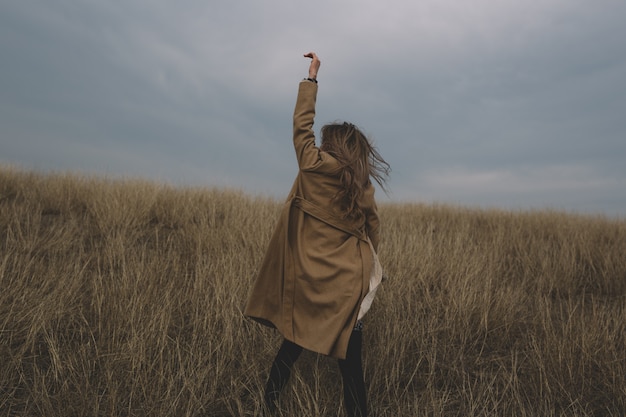 Foto eine frau, die in neutraler kleidung auf dem feld mit trockenem herbstgras gekleidet ist und einen blühenden schilfstrauß in den händen hält. modeporträt und wind weht ihr haar