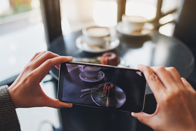 Foto eine frau, die mit dem handy ein foto von kaffee und snacks macht, bevor sie im café isst