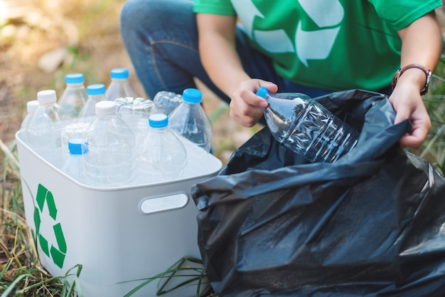 Eine Frau, die Müllplastikflaschen in eine Kiste und eine Plastiktüte für das Recyclingkonzept aufhebt