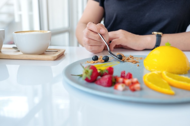 Eine Frau, die Orangenkuchen mit gemischten Früchten durch Löffel im Café isst