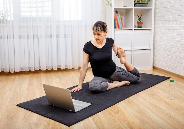 Eine Frau, die sich vor ihrem Laptop in einer Yogaposition ausdehnt