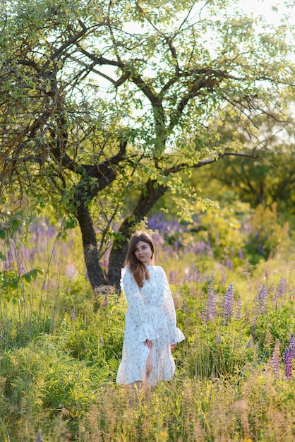 Eine Frau, die um Lupinblumen und einen Baum in einem Park spazieren geht