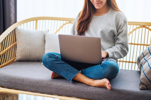 Eine Frau, die zu Hause auf einem Sofa sitzt und einen Laptop benutzt und daran arbeitet