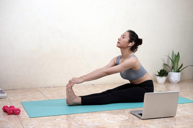 Eine Frau, die zu Hause Yoga mit Laptop macht