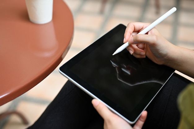 Eine Frau entspannt sich im Café im Freien mit einem tragbaren digitalen Tablet und nippt an Kaffee
