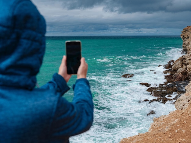 Eine Frau fotografiert das Meer auf dem Smartphone