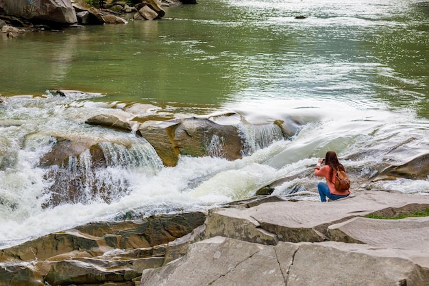 Eine Frau fotografiert einen Wasserfall an einem Gebirgsfluss