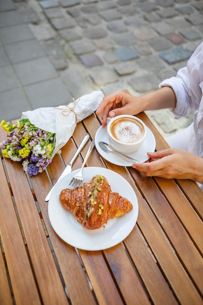 Eine Frau frühstückt auf der Terrasse, ein knuspriges Croissant und eine Tasse Kaffee
