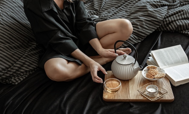 Eine Frau frühstückt mit Tee und Keksen und liegt an einem freien Tag im Bett