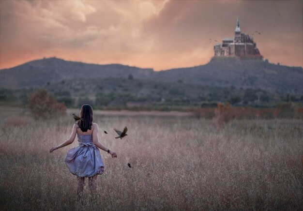 Eine Frau geht durch ein Feld, im Hintergrund fliegen Vögel.