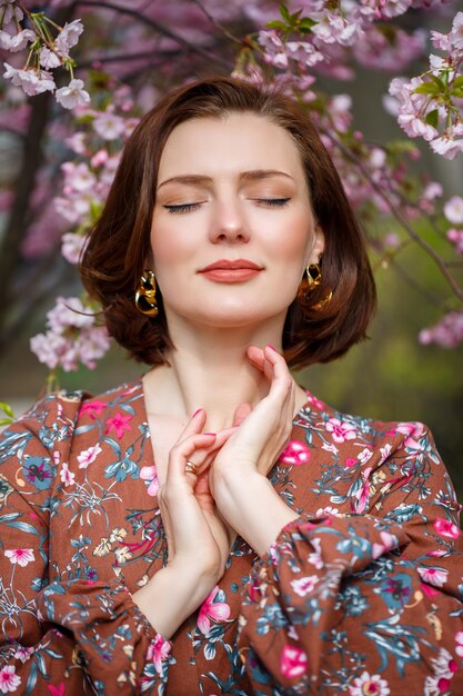 Eine Frau geht eine Frühlingsstraße entlang. Das Mädchen genießt den Duft eines blühenden Baumes. Schöne Frau in einem Kleid mit blühender Kirsche Sakura