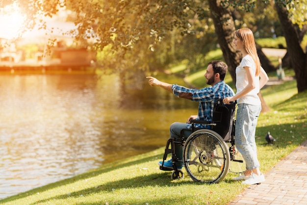 Eine Frau geht mit einem Mann im Rollstuhl in den Park