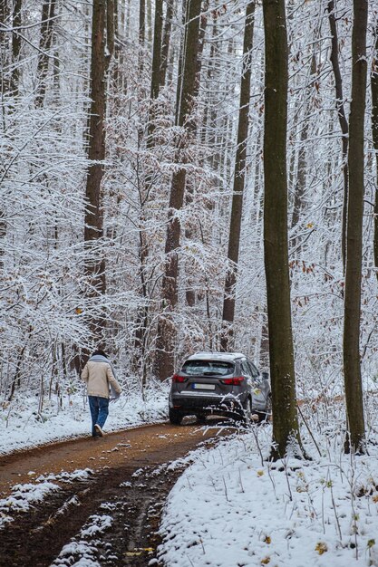 Eine Frau geht zu ihrem Auto, das zwischen schneebedeckten Bäumen auf einer Straße in einem Winterwald steht