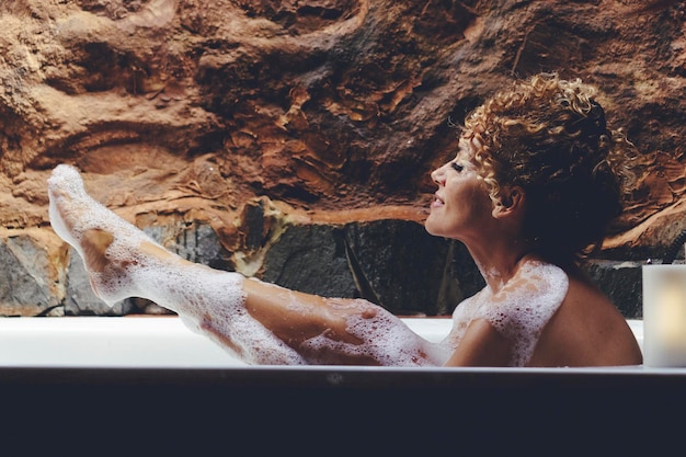 Eine Frau genießt ein Schaumbad Freizeitaktivität im Badezimmer zu Hause Körperpflege- und Hautbehandlungskonzept Weibliches Lächeln und Spaß beim Waschen in der Röhre Beine Enthaarungskonzept