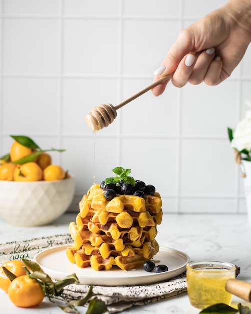 Eine Frau gießt Honig auf Wiener Waffeln mit Mandarinen Waffeln sind mit Minze verziert