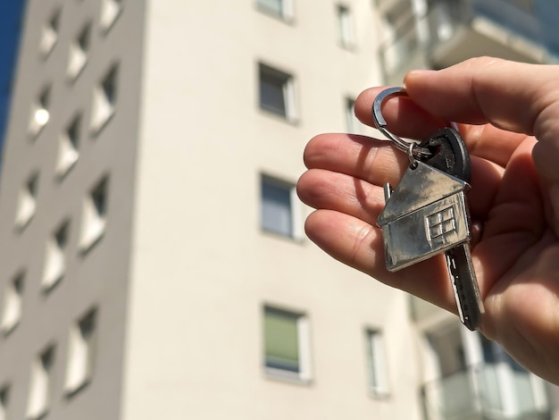 eine Frau hält die Schlüssel zum Haus gegen Hochhäuser Miet- oder Kaufkonzept