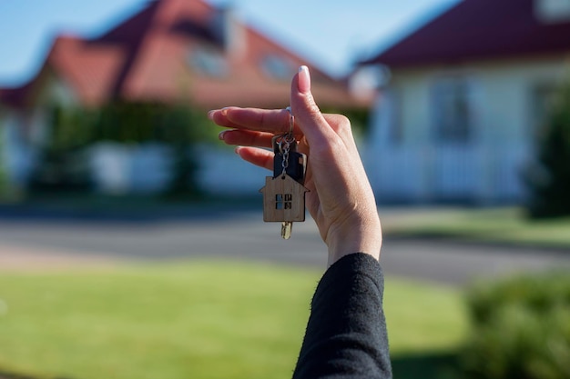 Eine Frau hält die Schlüssel zum Haus vor dem Hintergrund von Wohngebäuden in ihren Händen Konzept für den Kauf und die Anmietung von Wohnungen