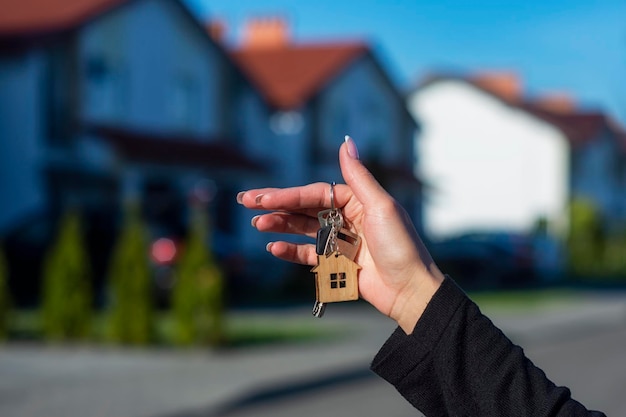 Eine Frau hält die Schlüssel zum Haus vor dem Hintergrund von Wohngebäuden in ihren Händen Konzept für den Kauf und die Anmietung von Wohnungen
