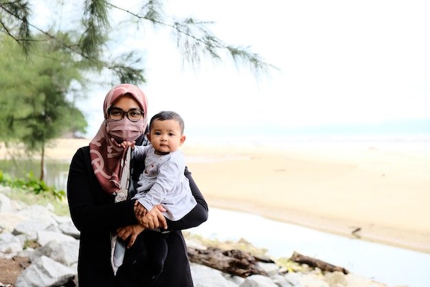 Eine Frau hält ein Baby vor einem Strand.