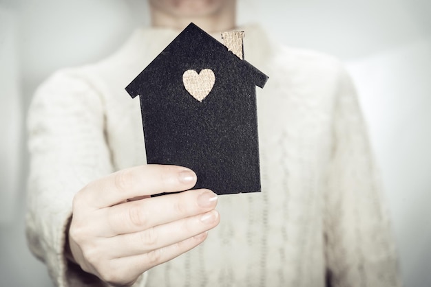 Eine Frau hält ein Modell eines dunklen Hauses in der Hand. Familien-, Immobilien- und Versicherungskonzept