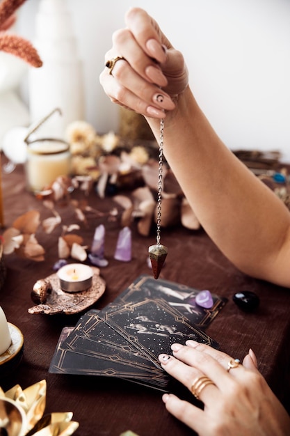 Eine Frau hält ein Pendel über das Tarotkartenspiel an ihrem herbstfarbenen Hexenaltar