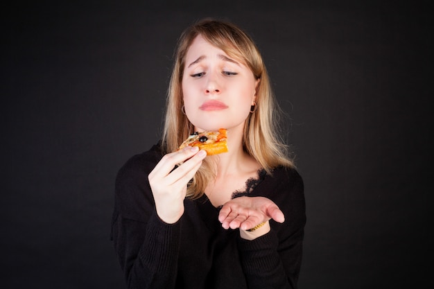 Eine Frau hält ein Stück Pizza in den Händen und schaut es fragend an.