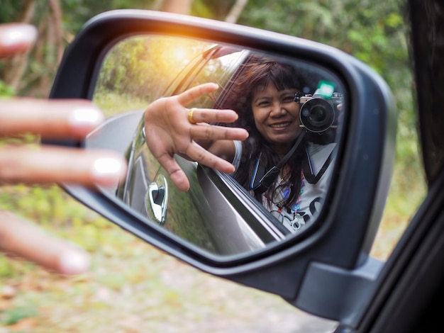 Eine Frau hält eine Digitalkamera in der Hand und fotografiert sich lächelnd im Autospiegel