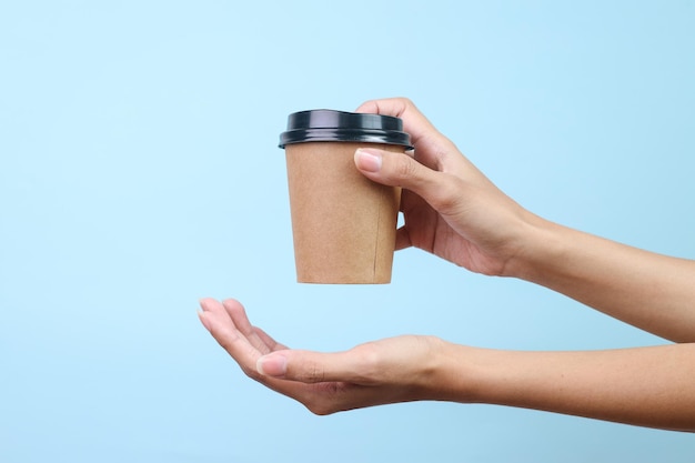 Eine Frau hält eine leere Kaffeepapiertasse für ein Modell in der Hand, das über einem blauen Hintergrund isoliert ist