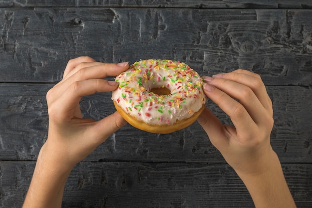 Eine Frau hält mit beiden Händen einen frischen Donut auf einem Holztisch