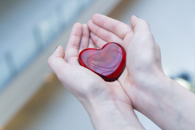 Eine Frau hält zum Valentinstag ein glasrotes Herz in den Händen oder spendet Hilfe, um Liebe zu wärmen