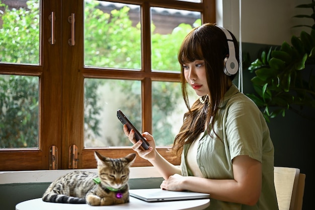 Eine Frau hört Musik über ihre Kopfhörer, während ihre süße getigerte Katze auf einem Tisch liegt